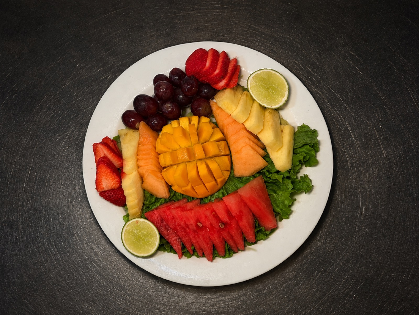 A fresh fruit platter at Manuel's — mango, watermelon, pineapple, cantaloupe, strawberries, grapes and lime over lettuce