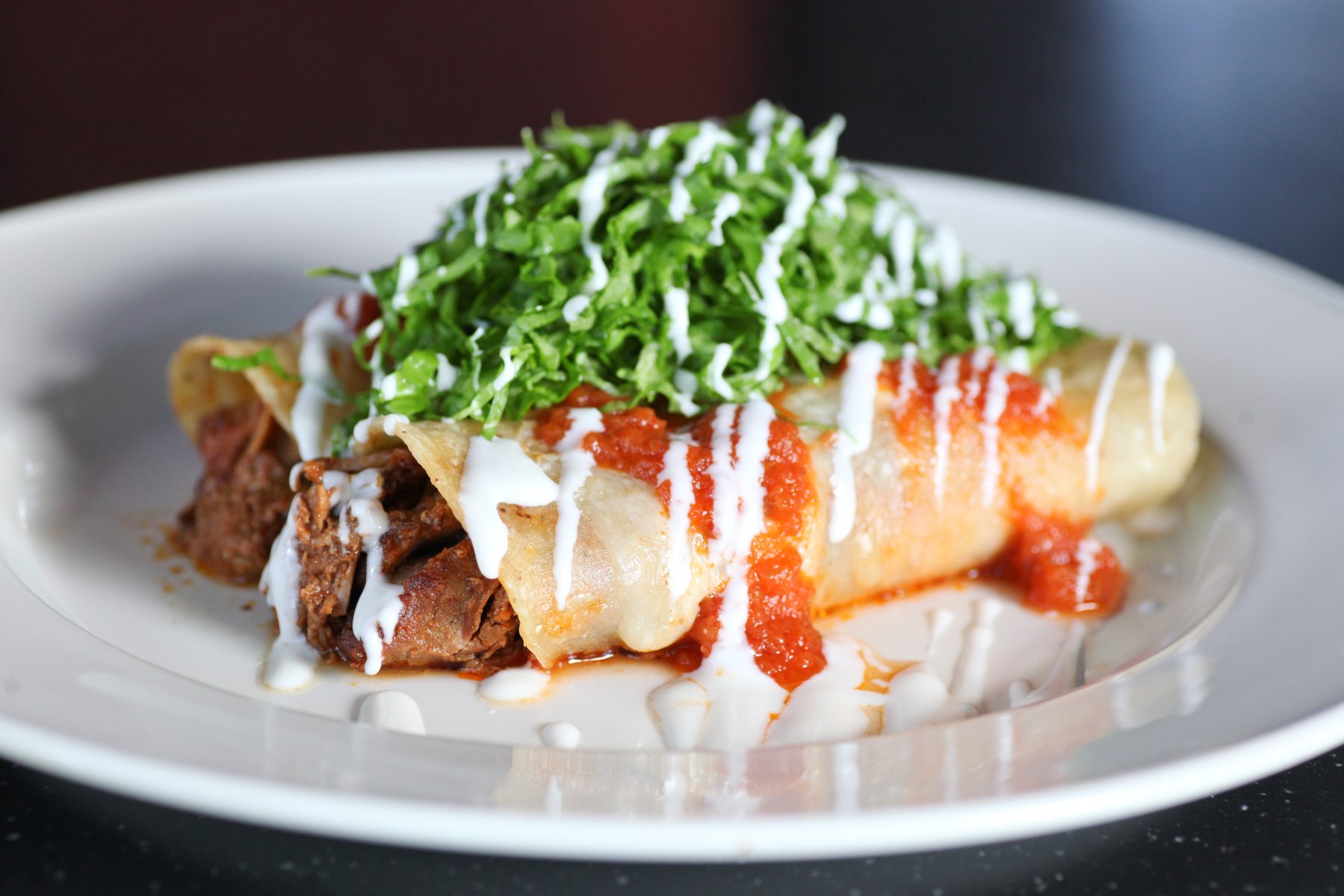 Enchiladas draped with crema, salsa roja and shredded lettuce