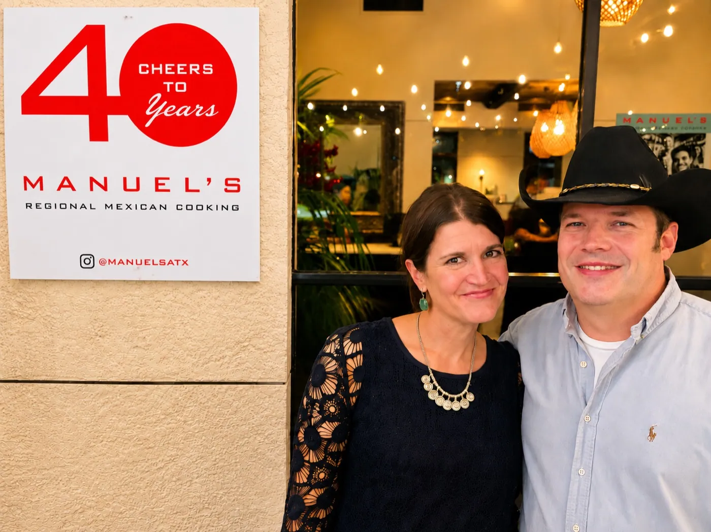 A couple celebrating beside Manuel's Cheers to 40 Years sign outside the restaurant