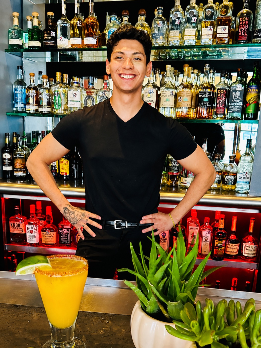 A Manuel's bartender smiling at the tequila bar beside a fresh mango margarita