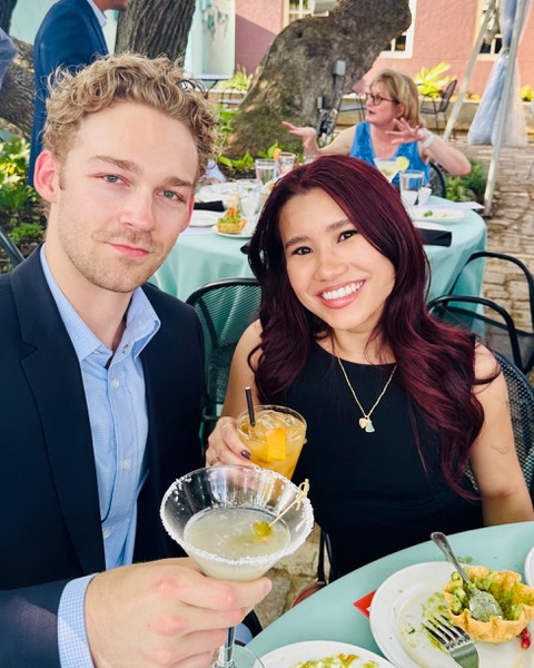 A couple toasting margaritas over their plates at a patio table at Manuel's
