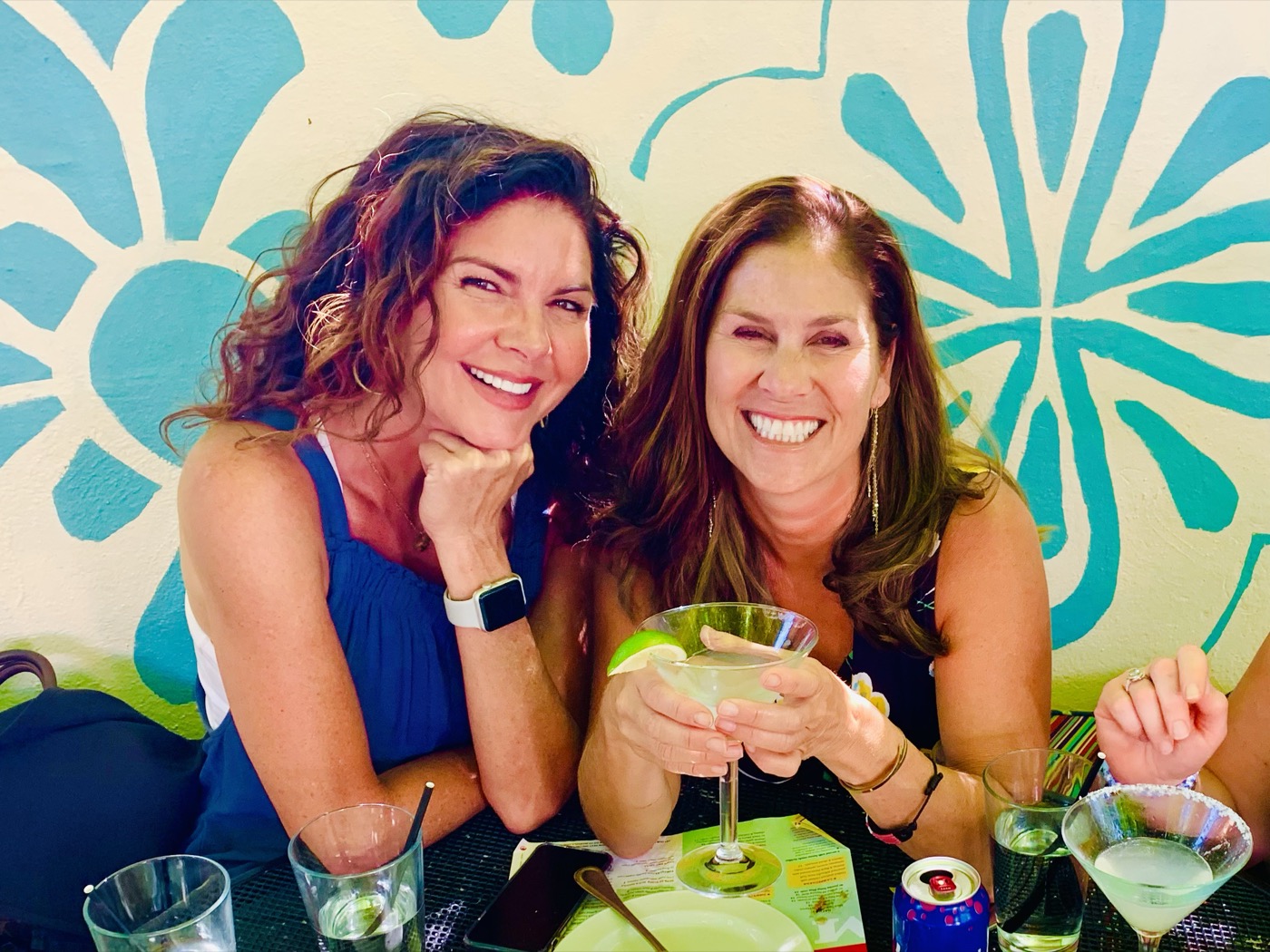 Two friends smiling over margaritas against Manuel's turquoise floral mural
