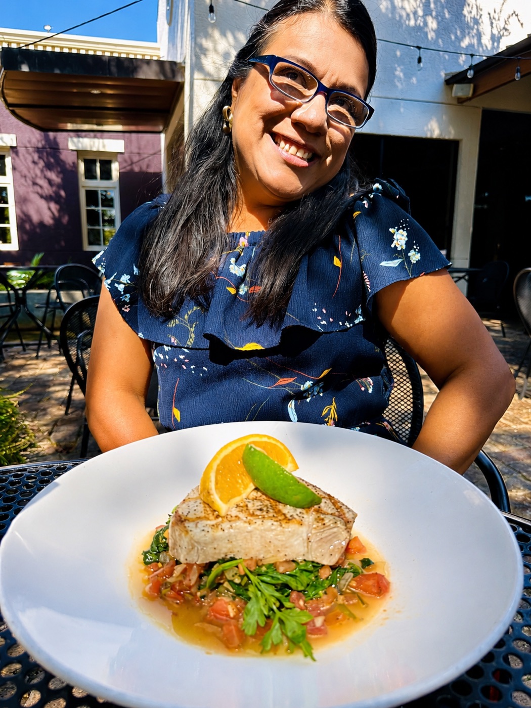 A guest smiling at a patio table over a plated grilled fish dish at Manuel's