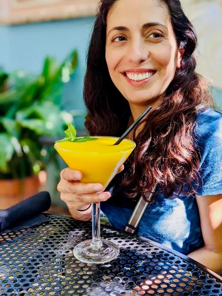 A guest on the patio smiling over a frozen mango margarita garnished with fresh mint at Manuel's