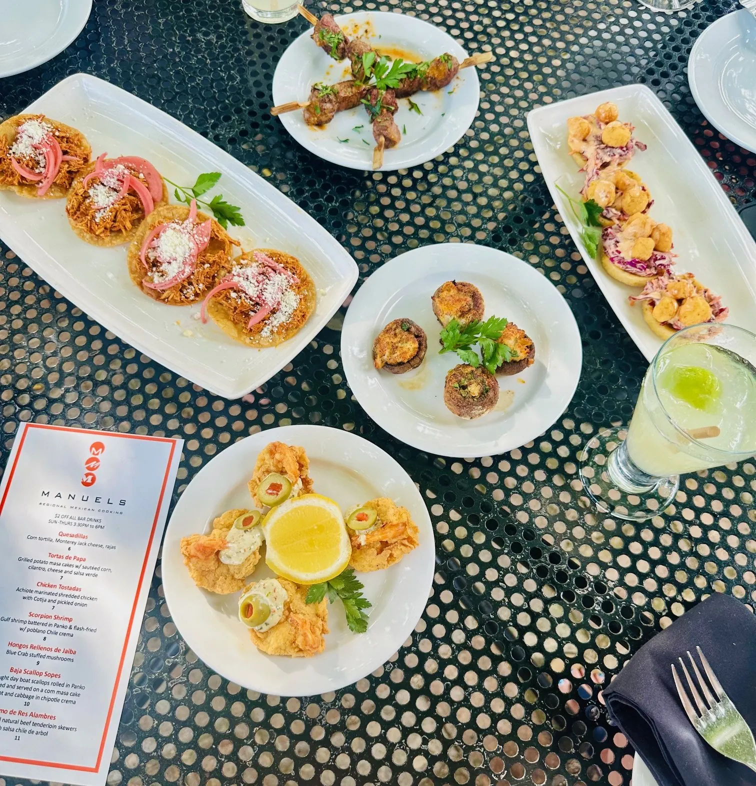 Happy hour spread beside the Manuel's menu card — chicken tostadas, beef brochettes, crab-stuffed mushrooms, scallop sopes, scorpion shrimp and a margarita