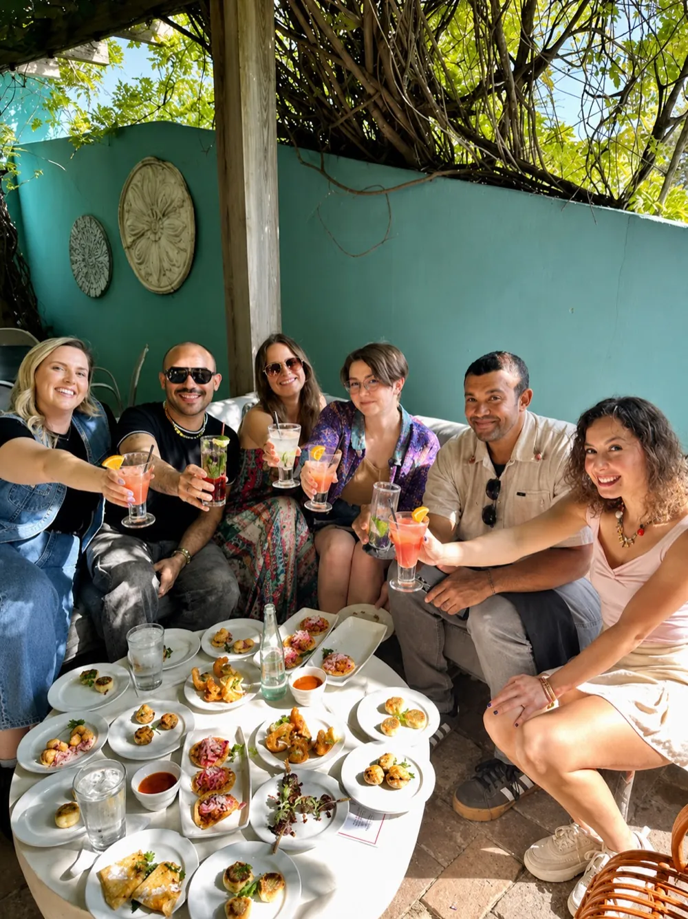 Friends raising cocktails over a spread of happy hour tapas on Manuel's turquoise-walled patio