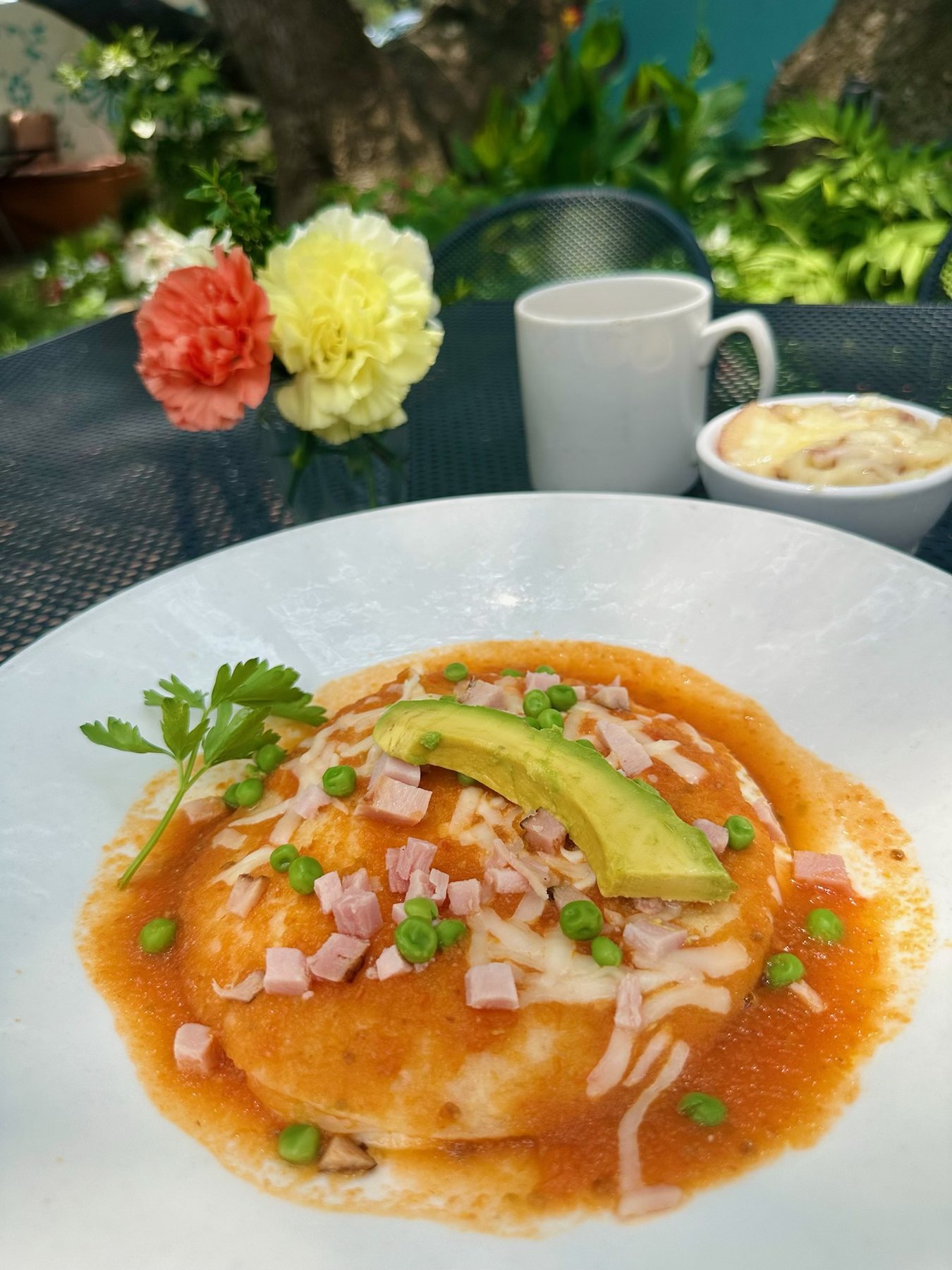 Huevos Motuleños — fried eggs on corn tortillas with black beans and salsa ranchera, topped with ham, peas and avocado