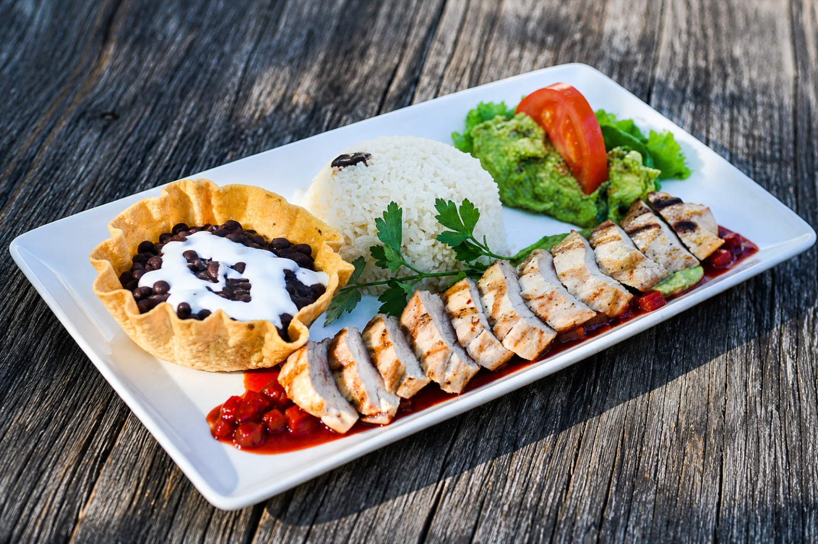 Lomo de Puerco — grilled sliced pork loin over red chile sauce with rice, black beans and guacamole