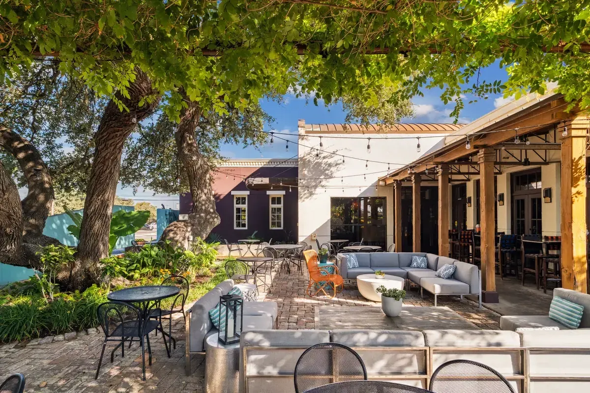 Manuel's shaded patio under the oaks — pergola lounge with sofas beneath the live oaks, set for an event