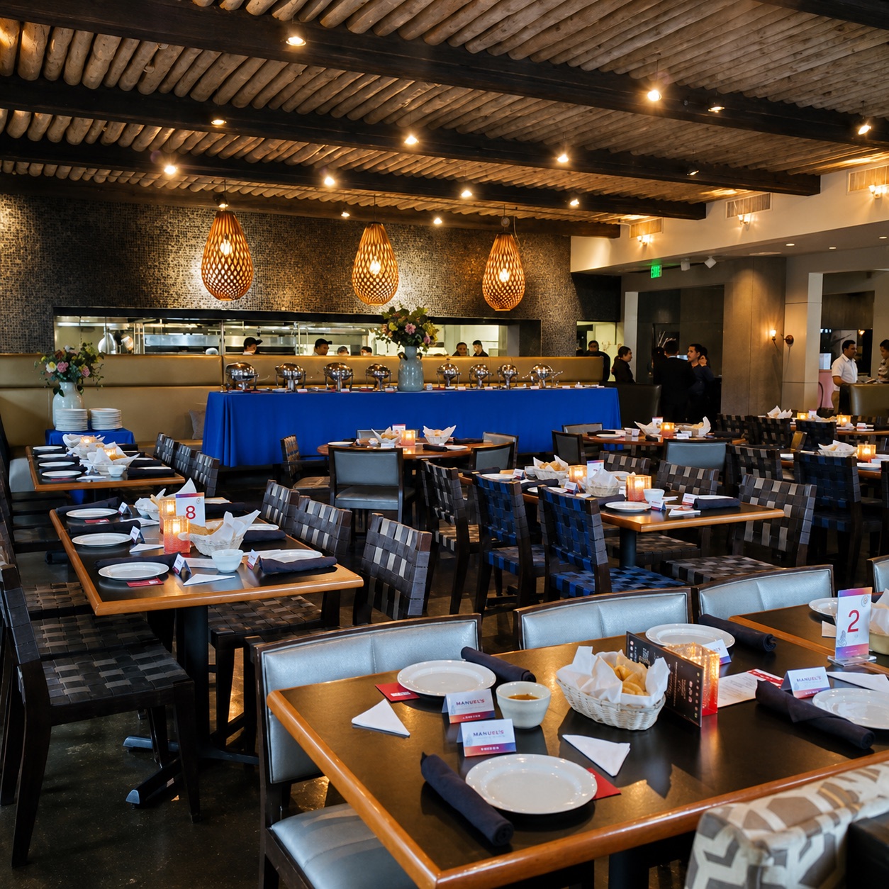 Manuel's party room set for a private event — a buffet with silver chafing dishes on a blue-draped table and place settings under the woven pendant lights