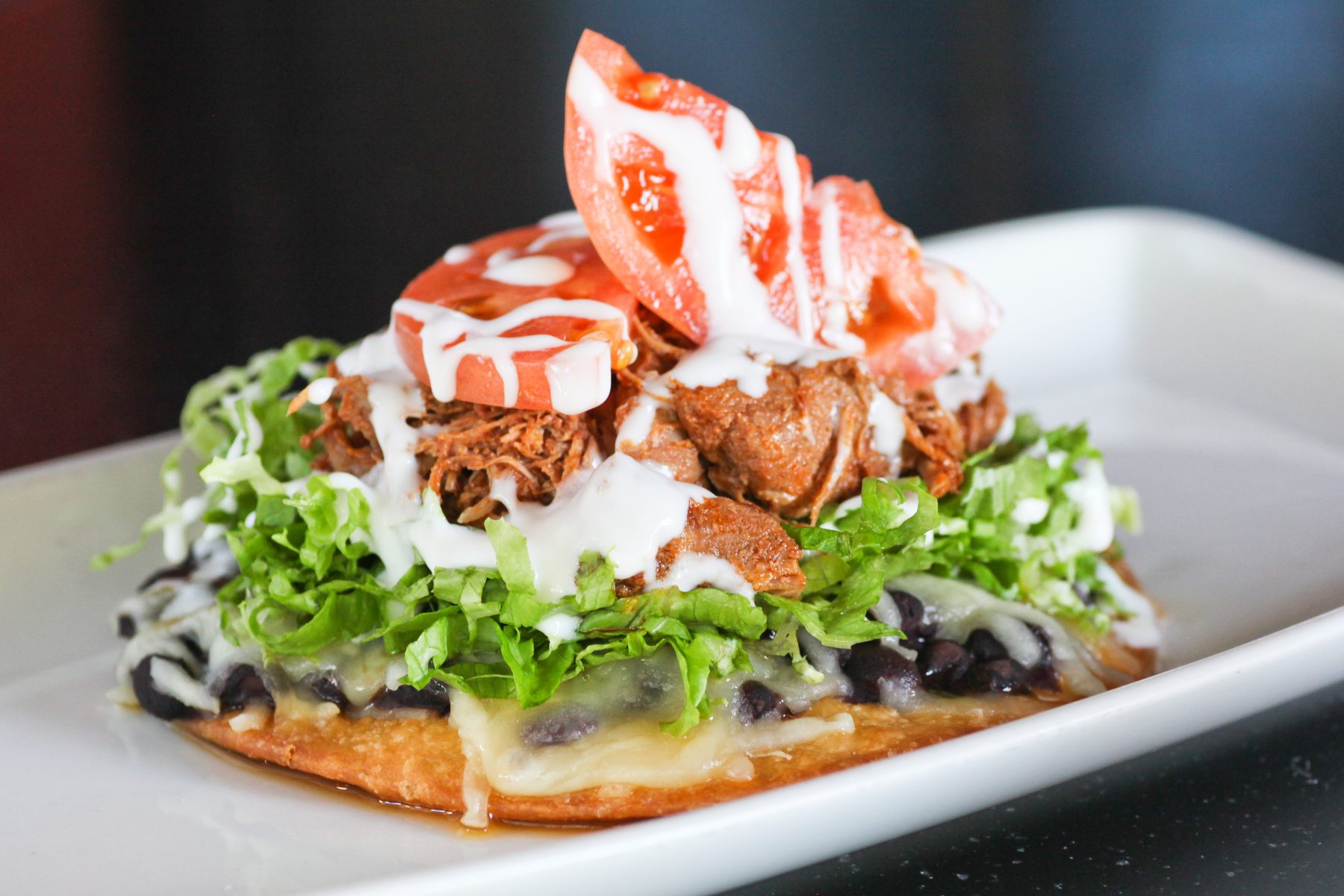 Crisp tostada piled with black beans, queso, lettuce, pork and tomato